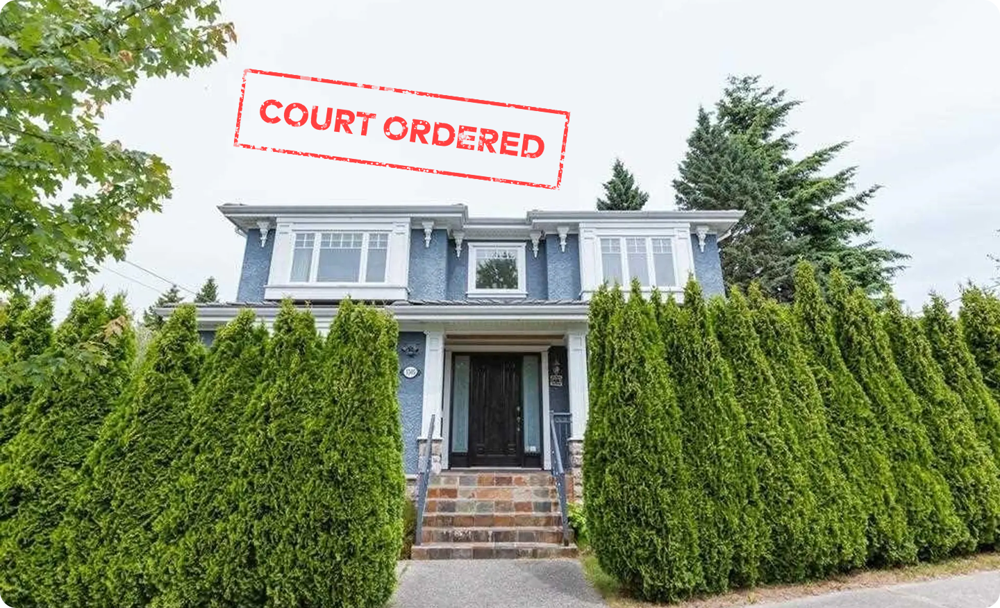 A blue two storey Vancouver Westside house behind tall cedar hedges and stone front steps, stamped Court Ordered in red across the top of the photograph